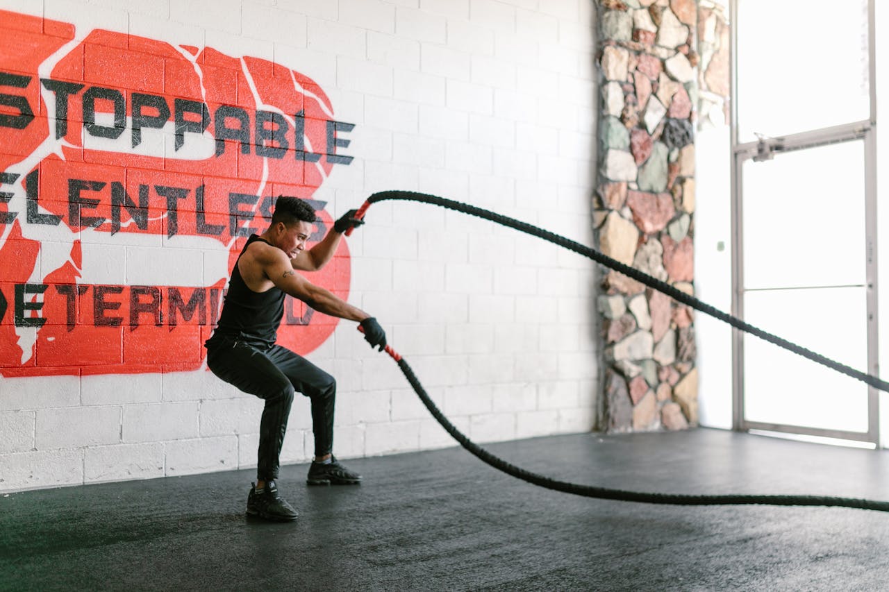 Athletic man training with battle ropes in a gym with motivational wall art.